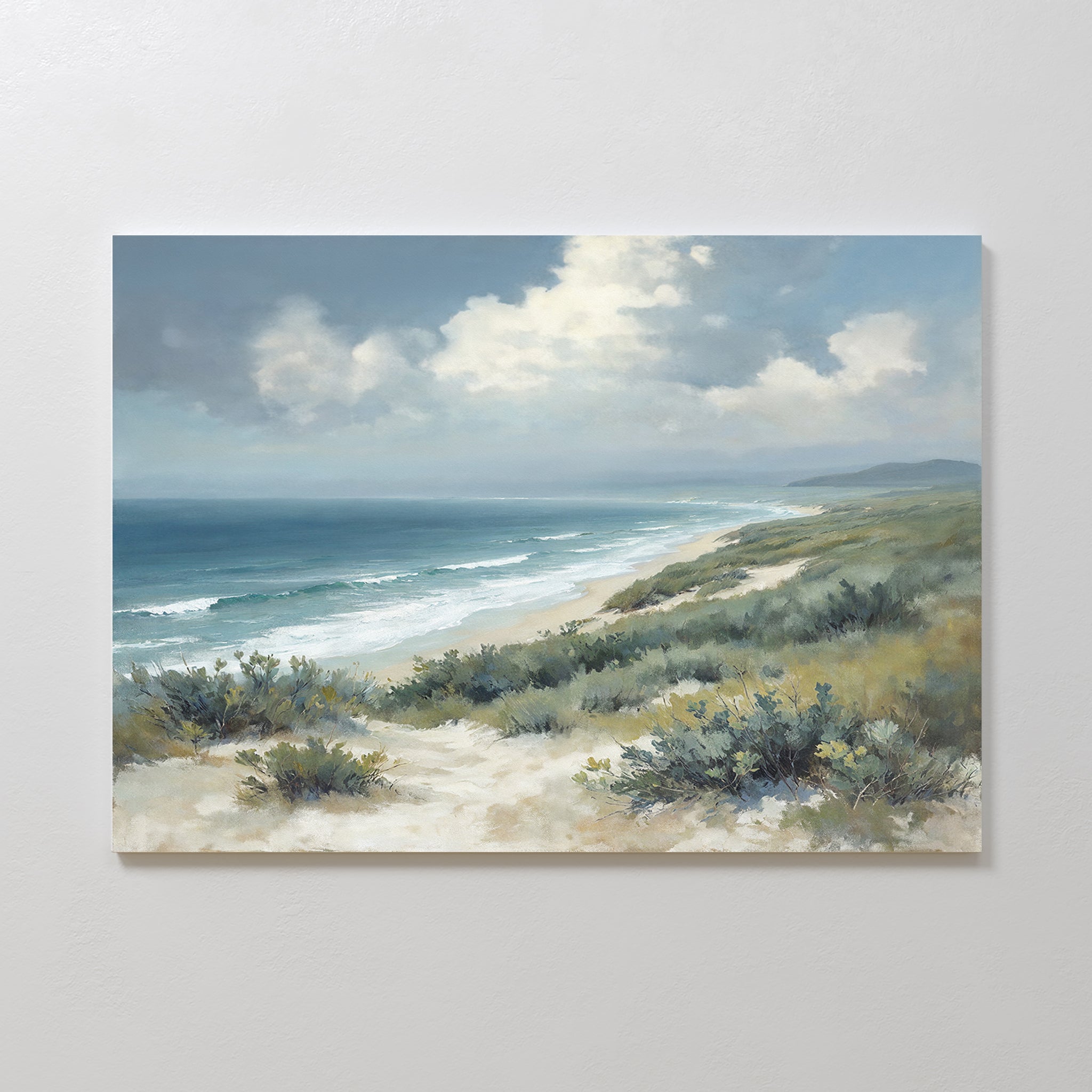 The Ocean Bluff Canvas Art - Horizontal features a serene coastal scene with waves on a sandy beach, blue ocean, cloudy sky, and green shrubs—a beautiful seaside artwork.