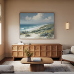 A cozy living room with a light wood sideboard, the Ocean Bluff Canvas Art - Horizontal above it, a modern oval coffee table, beige rug, light sofa, and a small vase of flowers on the table.