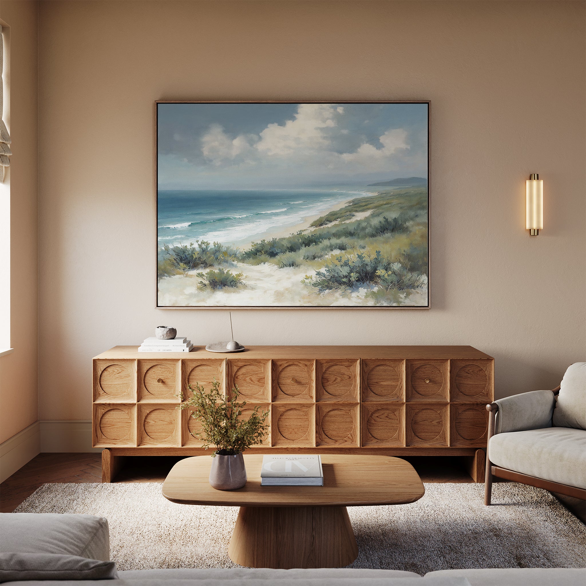 A cozy living room with a light wood sideboard, the Ocean Bluff Canvas Art - Horizontal above it, a modern oval coffee table, beige rug, light sofa, and a small vase of flowers on the table.
