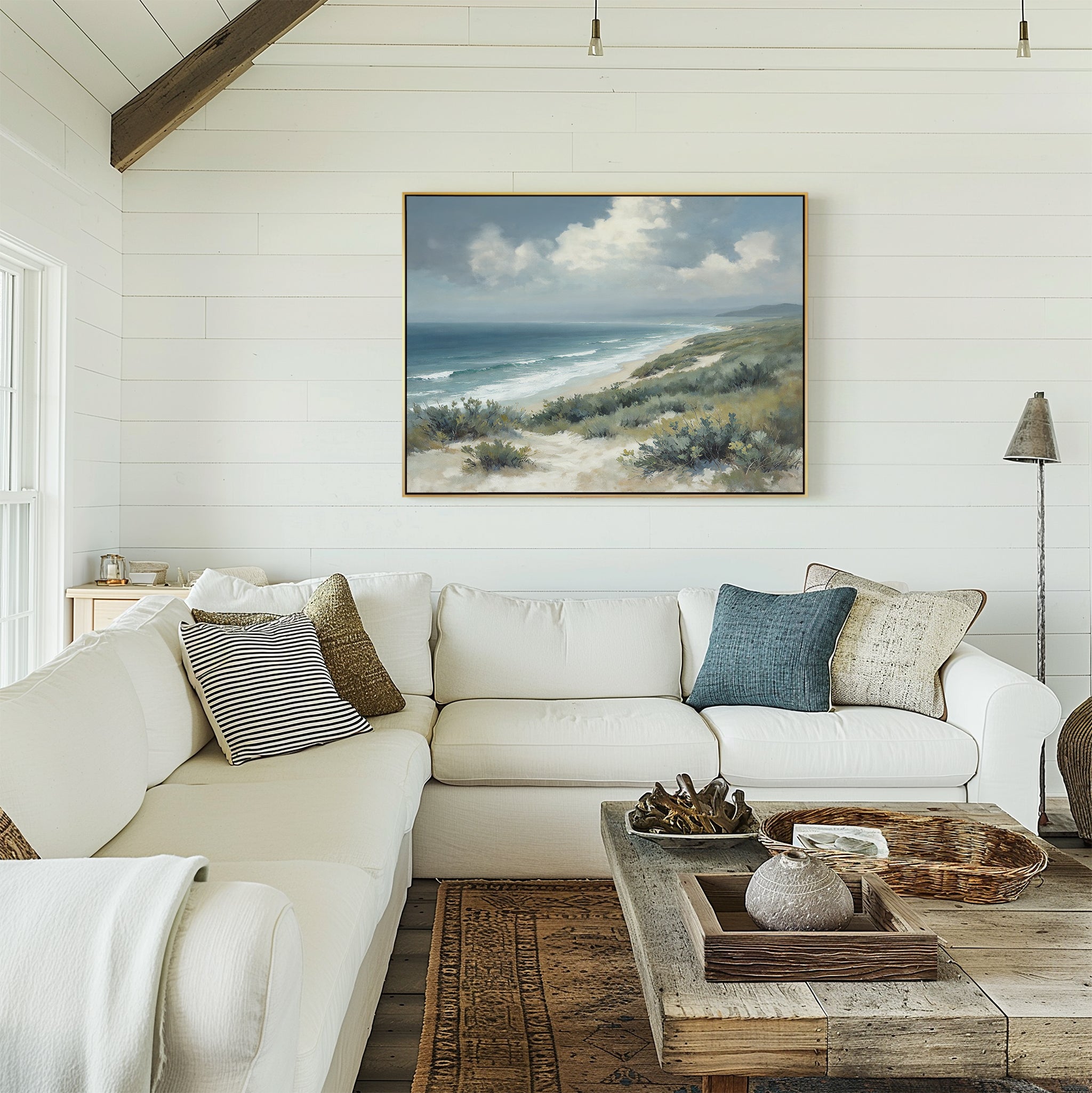 A bright, cozy living room with white shiplap walls, a large white sectional sofa with cushions, a rustic wooden coffee table, and the Ocean Bluff Canvas Art - Horizontal hanging above the couch.