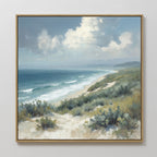 The Ocean Bluff Canvas Art - Square features a framed coastal scene of a sandy beach with green shrubs, gentle waves, distant hills, and a partly cloudy sky, all captured in soft natural light for a serene touch to your space.