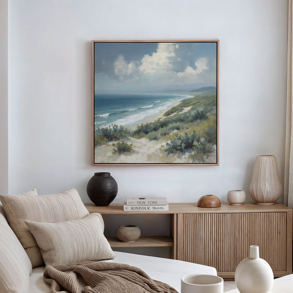 A cozy living room with neutral tones features a sofa with beige cushions, a wooden sideboard adorned with decor, and the Ocean Bluff Canvas Art - Square displayed on the wall.