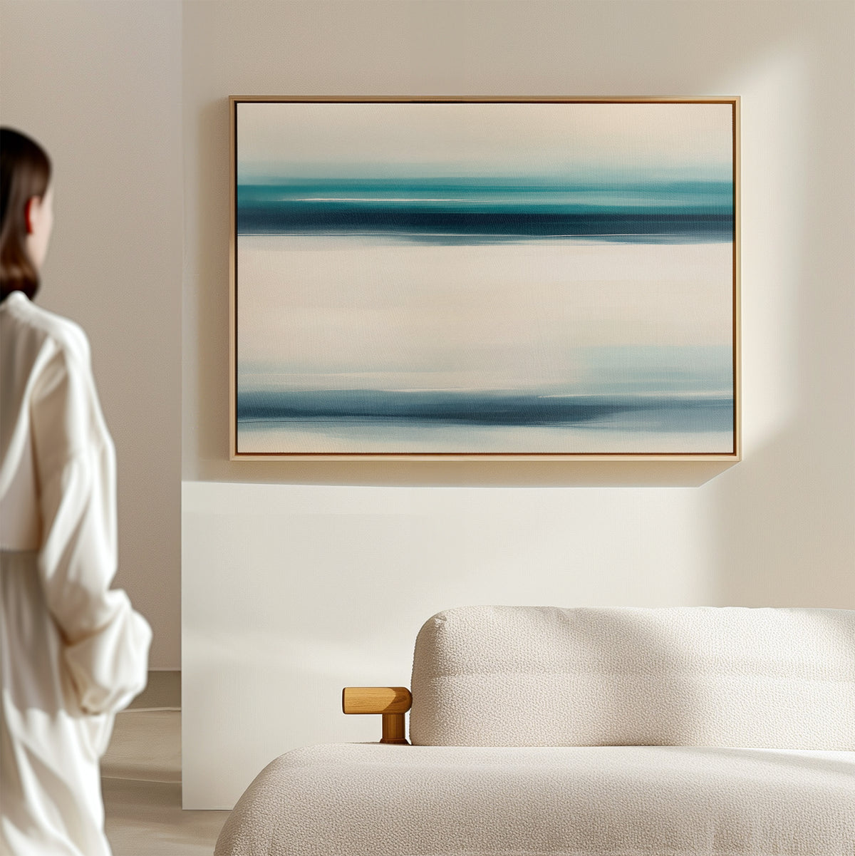 A person admires the Ocean Motion Canvas Art - Horizontal, featuring blue, turquoise, and white bands above a light sofa in a minimalistic room, creating a serene and subtly coastal ambiance with sophisticated style.