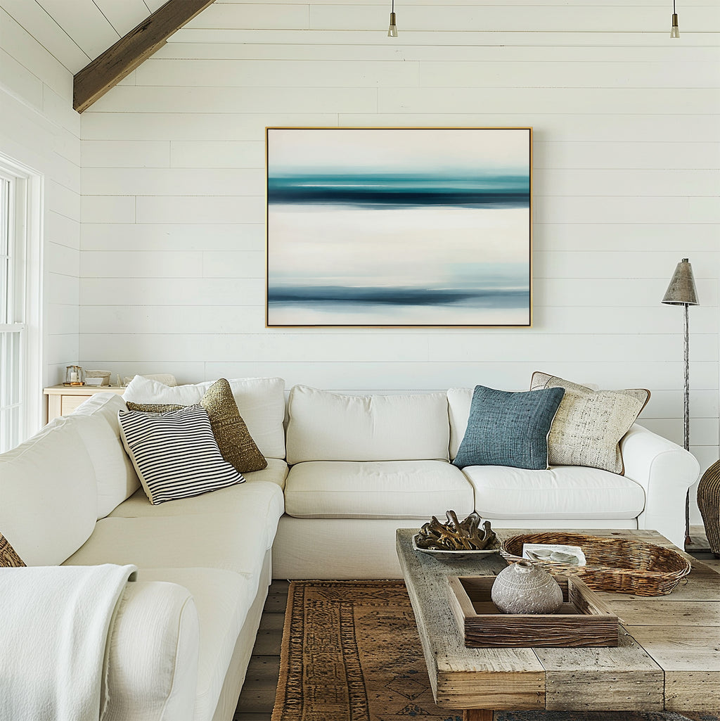 A bright living room with a white sectional sofa, mixed pillows, a rustic wooden coffee table, and the Ocean Motion Canvas Art - Horizontal on the shiplap wall exudes serene sophistication as warm light streams in from the left.