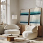 A modern living room with two white rounded armchairs, a low wooden coffee table, and a sideboard. The Ocean Motion - Set Of 2 abstract blue and white paintings add serene sophistication, while large windows bring in natural light.