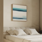 A modern bedroom features a beige upholstered bed with white bedding and pillows. Above, the Ocean Motion Canvas Art - Square showcases blue and teal brushstrokes, adding serene sophistication to the calm, minimalist space.