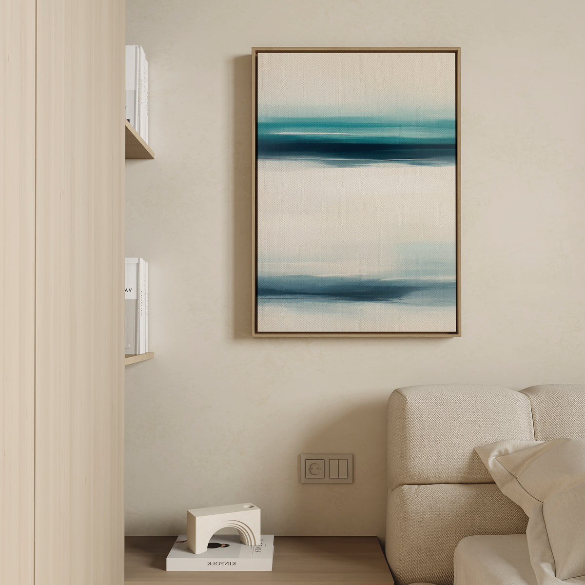 A minimalist living room features a beige sofa, shelves with books and a white decor piece, and the Ocean Motion Canvas Art - Vertical, displaying abstract blue, teal, and white brushstrokes on a cream-colored wall.
