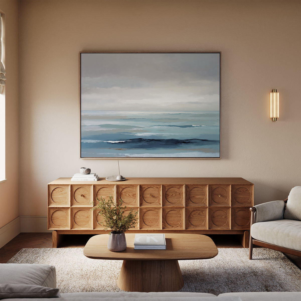 A modern living room with neutral walls, a light sofa, wooden coffee table, textured sideboard, and the Ocean Swells Canvas Art - Horizontal above. Tables are decorated with a small plant and books.