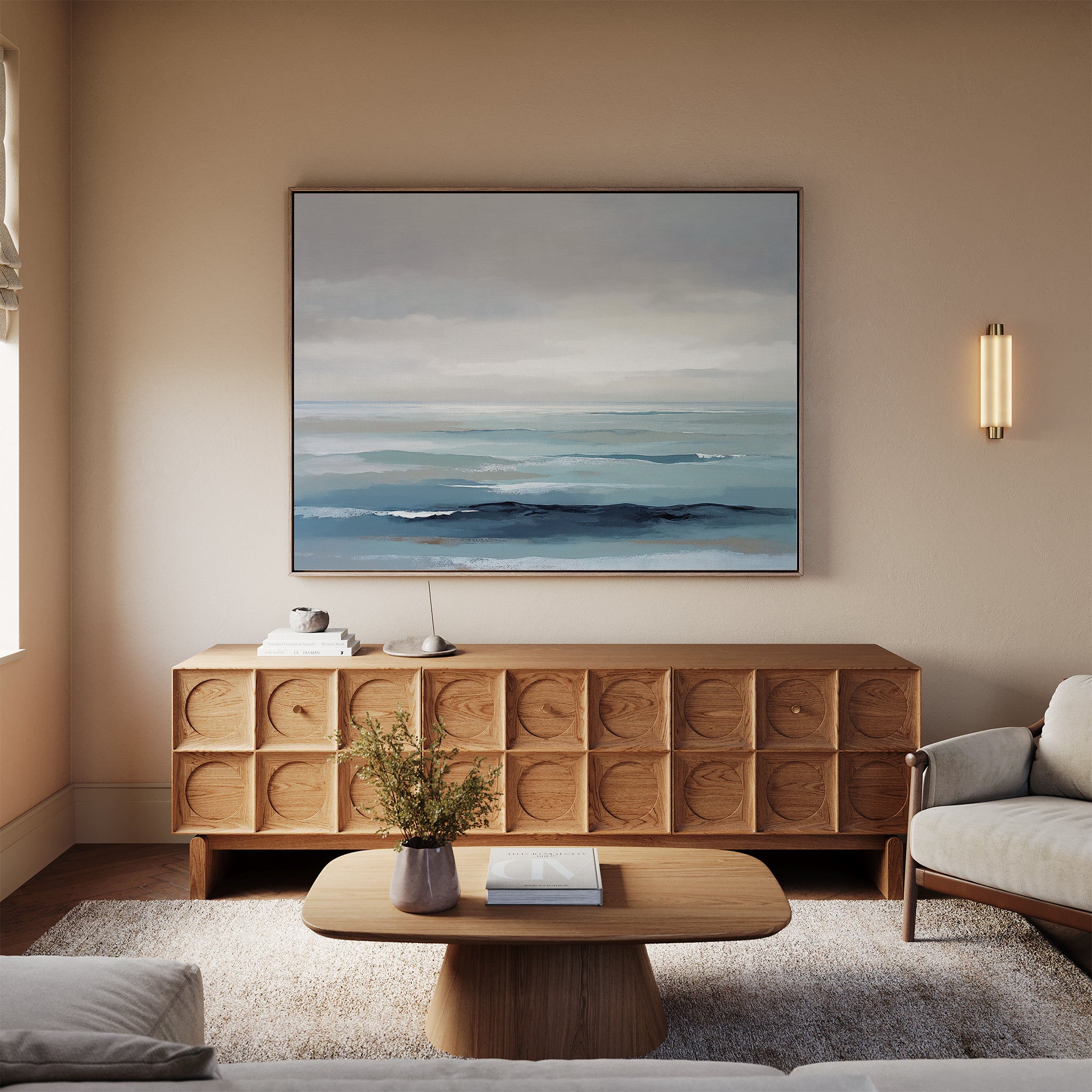 A modern living room with neutral walls, a light sofa, wooden coffee table, textured sideboard, and the Ocean Swells Canvas Art - Horizontal above. Tables are decorated with a small plant and books.