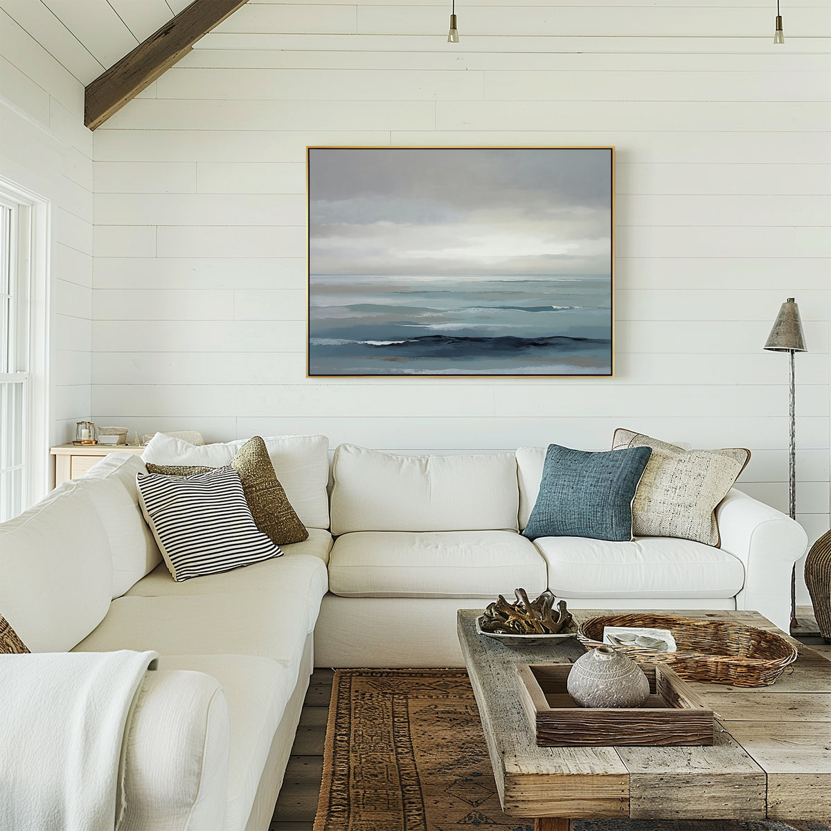 A bright, cozy living room with a white sectional sofa, assorted throw pillows, a rustic wooden coffee table, and the Ocean Swells Canvas Art - Horizontal on a white shiplap wall. Natural light fills the space.