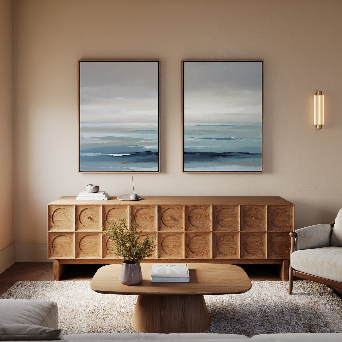 A modern living room with a wooden sideboard, a coffee table with books and a vase, a light sofa, and the "Ocean Swells - Set Of 2" serene abstract landscape wall art displayed above the sideboard.