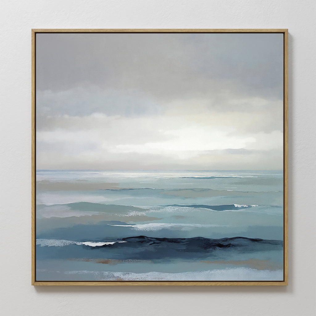 The Ocean Swells Canvas Art - Square features a framed coastal print of calm blue and gray waves under a cloudy sky, blending soft, muted tones for a tranquil, minimalist look—ideal serene wall art for any space.