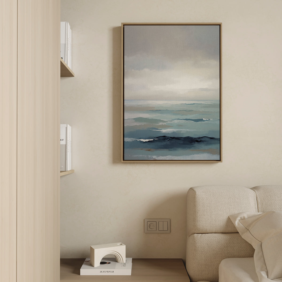 The Ocean Swells Canvas Art - Vertical, depicting blue waves and a cloudy sky, hangs above a light sofa in this serene living room. Books and a decorative object on nearby shelves enhance the Nordic Park-inspired decor.