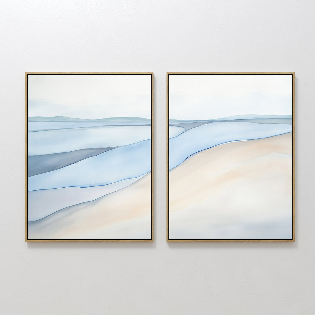 The "Pale Currents - Set of 2" features two framed abstract canvas prints in soft blue, beige, and gray tones, evoking a serene seascape with gentle waves and sandy shores, perfect for adding a calming touch to any white wall.