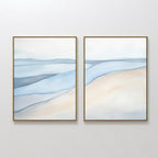 The "Pale Currents - Set of 2" features two framed abstract canvas prints in soft blue, beige, and gray tones, evoking a serene seascape with gentle waves and sandy shores, perfect for adding a calming touch to any white wall.