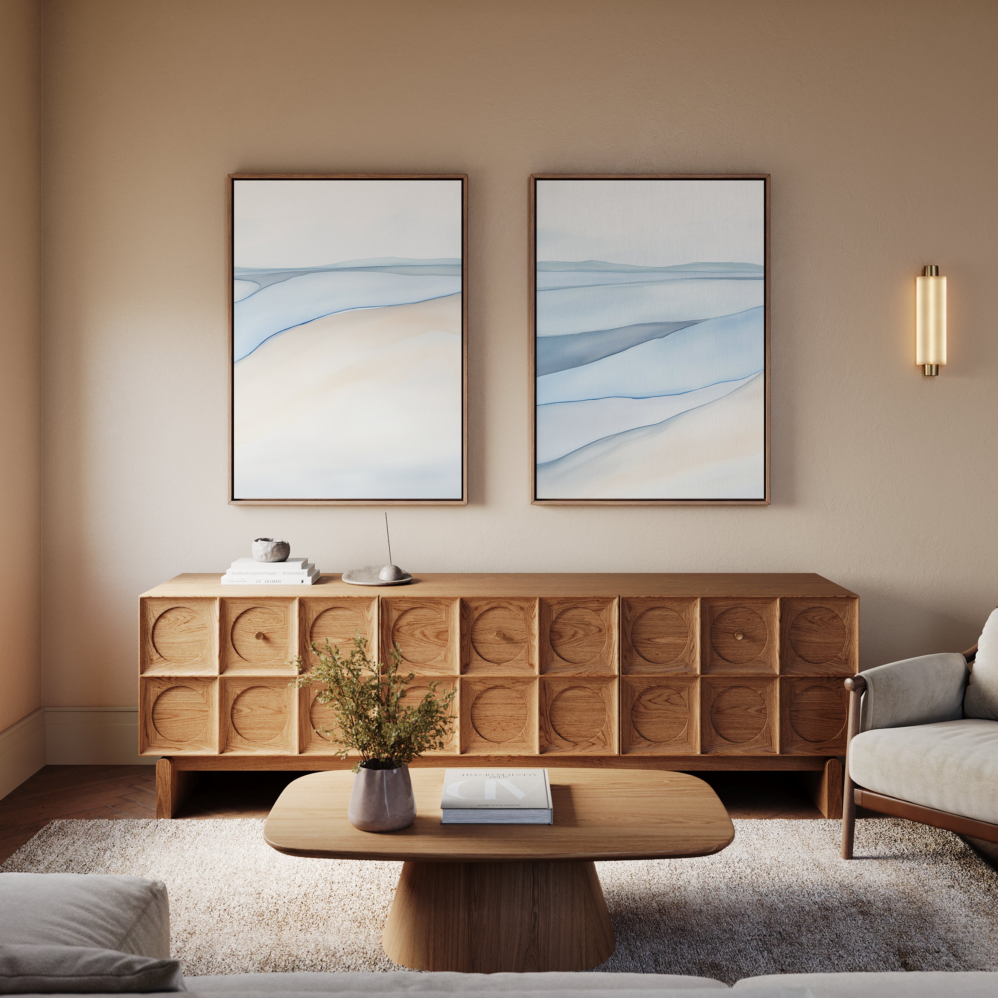 A modern living room featuring a wooden sideboard, Pale Currents - Set of 2 abstract canvas prints in blue and beige, a wooden coffee table with a plant and books, and a light gray sofa—ideal for your Nordic Park-inspired retreat.