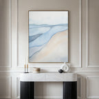 A minimal, modern console table with decor stands against a paneled beige wall, topped by Pale Currents Canvas Art - Vertical—an abstract print in soft blue, beige, and white evoking a serene Nordic park landscape.