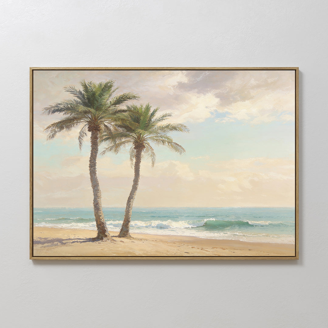 The Paradise Found Canvas Art - Horizontal, featuring two palm trees on a sandy shore with gentle waves and a partly cloudy sky, hangs on a white wall to add serene beach-themed decor to your space.