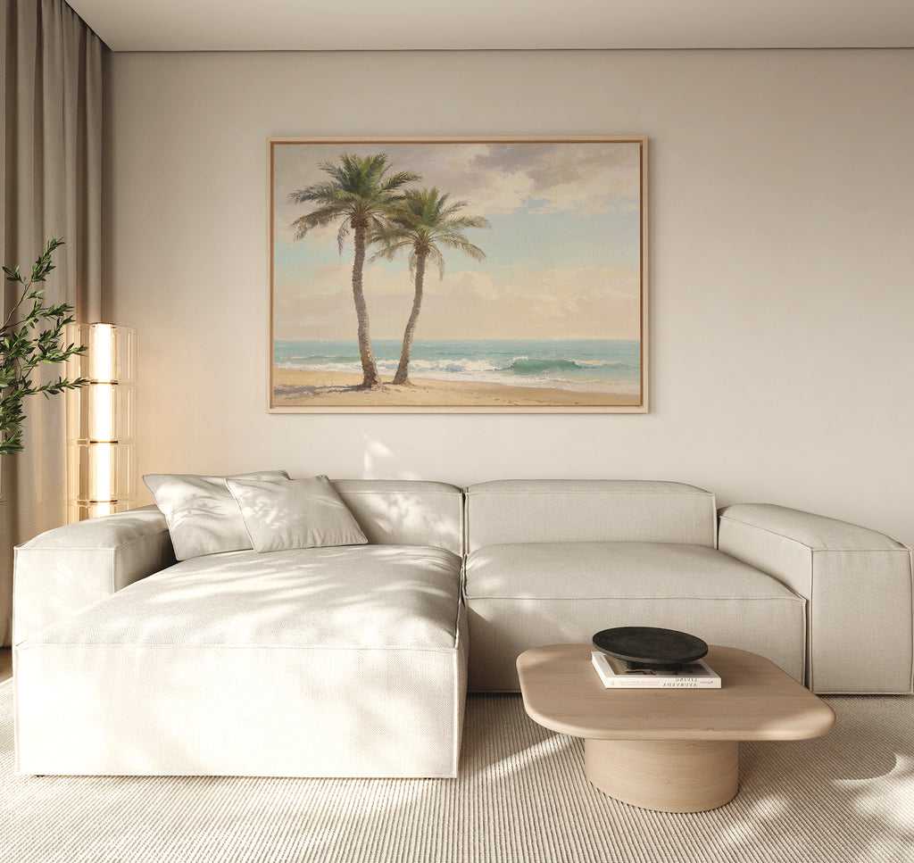 A modern living room with a light beige sectional, wooden coffee table, and the Paradise Found Canvas Art - Horizontal depicting palm trees and a beach. Neutral tones and natural light complete the serene, coastal-inspired space.