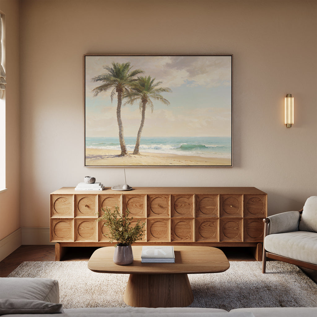 A cozy living room features a wooden coffee table, light sofa, textured sideboard, and the Paradise Found Canvas Art - Horizontal above it. Warm neutrals and coastal artwork create an inviting, relaxed atmosphere.