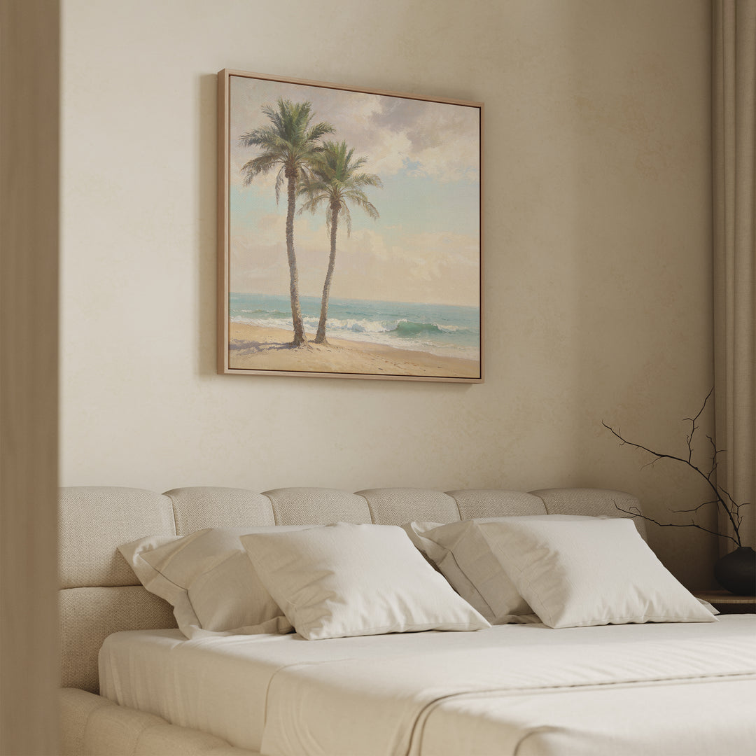 A serene bedroom features a beige upholstered bed, white pillows, and the Paradise Found Canvas Art - Square depicting two palm trees on a beach, glowing in soft natural light and complemented by minimalist decor.