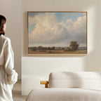 A person in a white shirt admires the 'Pastoral Grandeur Canvas Art - Horizontal' depicting a cloudy sky and open fields, displayed above a light sofa in this minimalist, Nordic Park-inspired room.