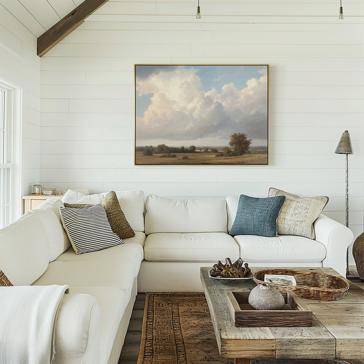 A bright, cozy living room with white shiplap walls, a large sectional sofa with assorted pillows, a rustic wooden coffee table, and the Pastoral Grandeur Canvas Art - Horizontal hanging above the couch.