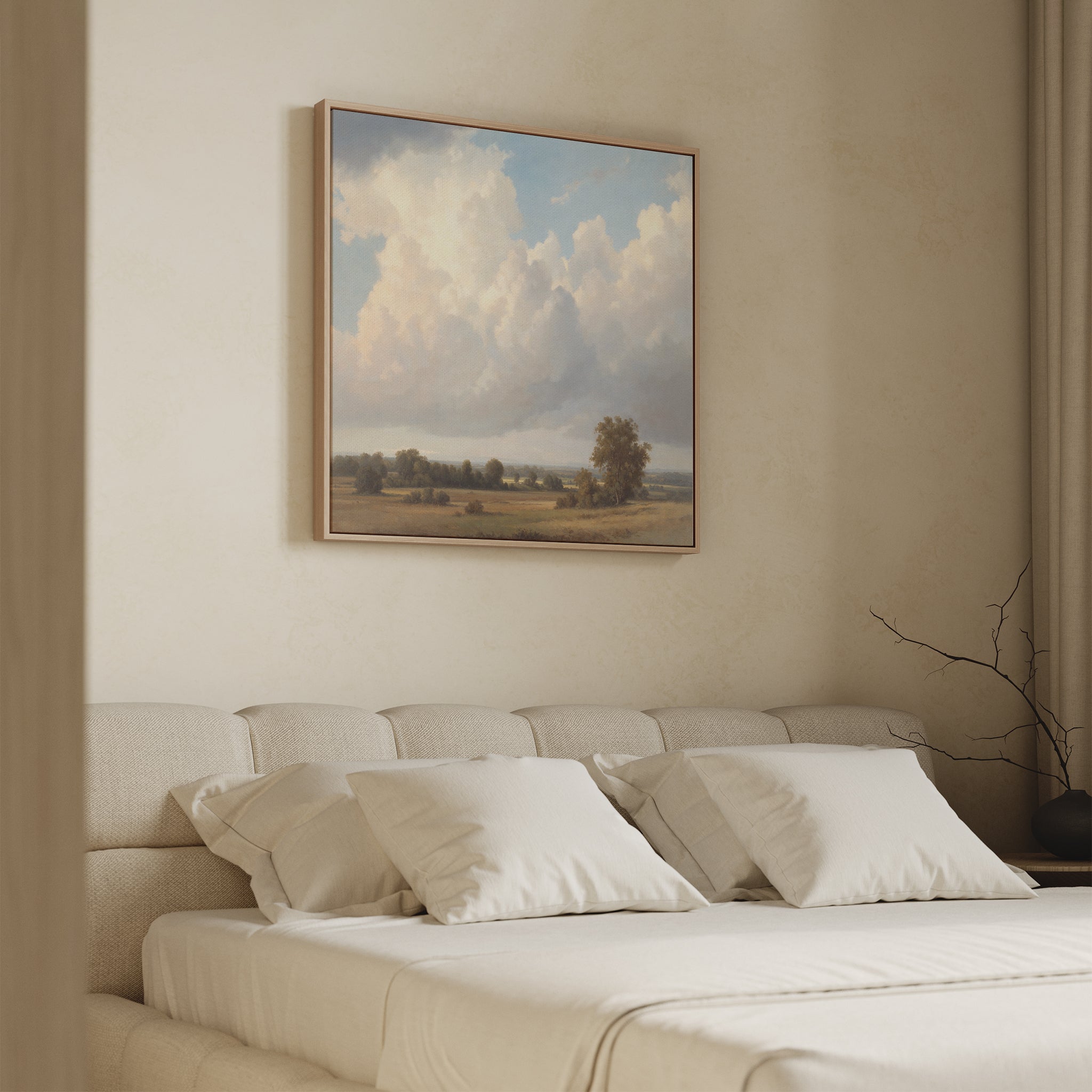 A minimalist bedroom with a beige upholstered bed, white pillows, and the Pastoral Grandeur Canvas Art - Square depicting clouds and fields above the headboard on a light wall. A bare branch in a vase adorns the nightstand.