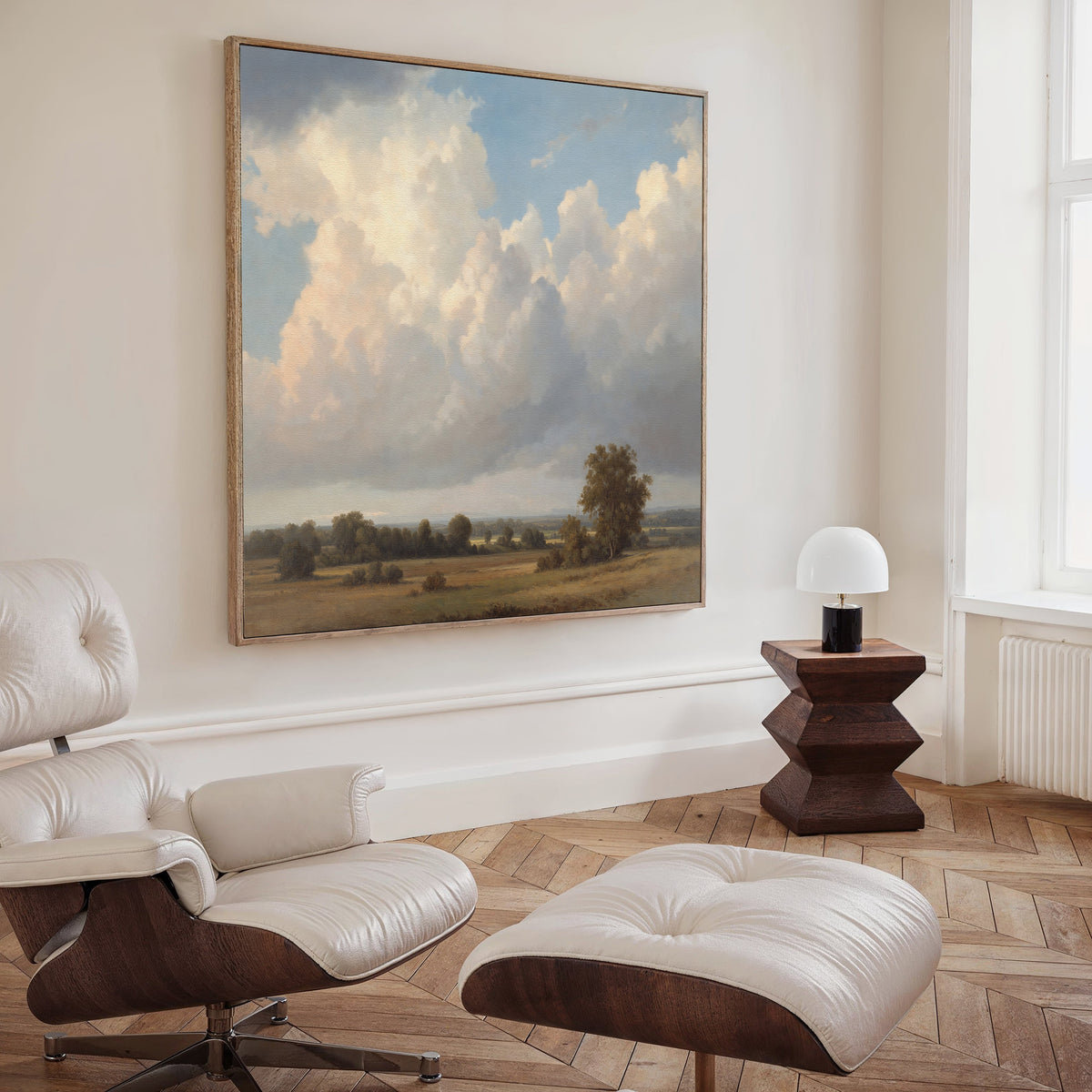 A minimalist living room with a white lounge chair and ottoman, a geometric wood side table with lamp, and the Pastoral Grandeur Canvas Art - Square as serene wall decor above elegant wooden herringbone floors.