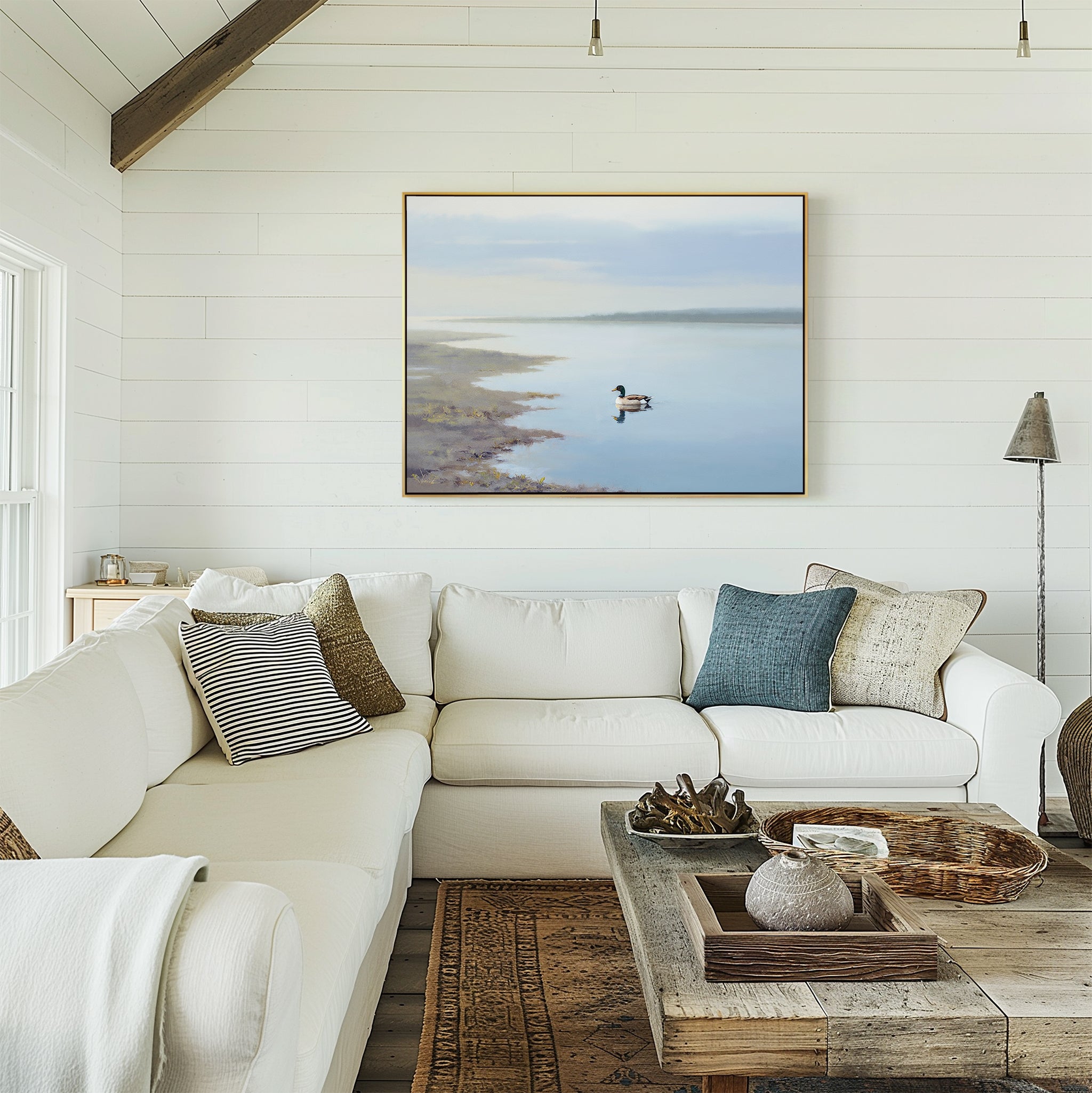 A bright, cozy living room with white shiplap walls, a large white sectional sofa with assorted pillows, a rustic wooden coffee table, and the Peaceful Duck Haven Canvas Art - Horizontal displayed above the couch.