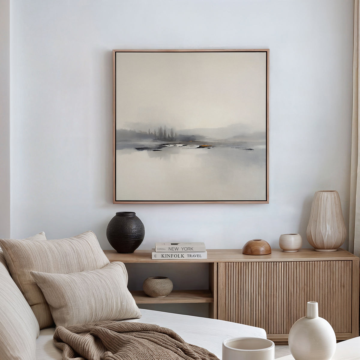 A minimalist living room with a light sofa, neutral cushions, wooden sideboard, ceramic vases, books, and the Peaceful Lake Morning Canvas Art - Square on a white wall creates a serene atmosphere.