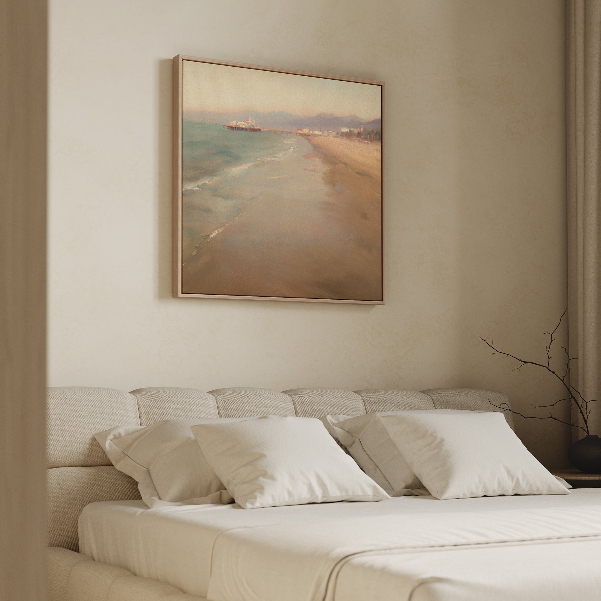 A minimalist bedroom with a beige upholstered bed and white bedding features the Pier Dreams Canvas Art - Square, showcasing a serene beach scene above the headboard. A bare branch on the bedside table enhances this coastal vibe.