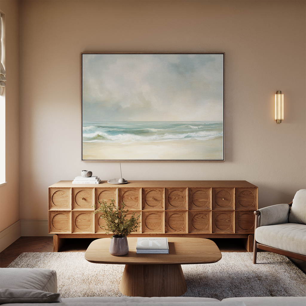 A cozy living room features a light sofa, wooden coffee table, textured sideboard, and the Serene Beach Canvas Art above. A small plant and books on the coffee table enhance the vintage decor charm.