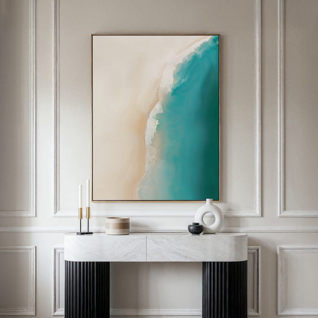 A minimalist room with a white marble console table, decorative accents, and The Beach Abstract Canvas Art—a large framed piece showing an abstract aerial view of sandy shore meeting turquoise sea.