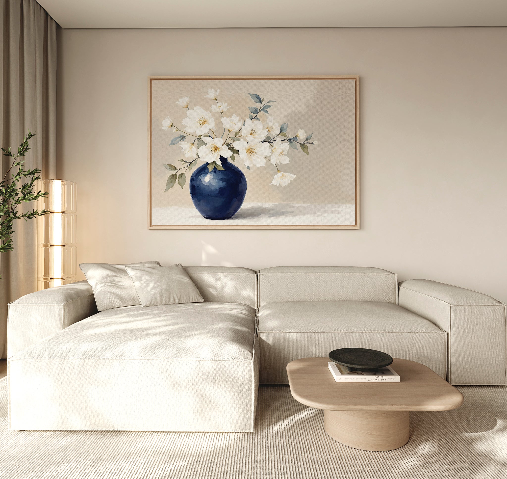 A modern living room features a light beige sectional sofa, a low wooden coffee table, and the Porcelain Dreams Canvas Art - Horizontal of white flowers in a blue vase on the wall, illuminated by soft natural light in a minimalist setting.