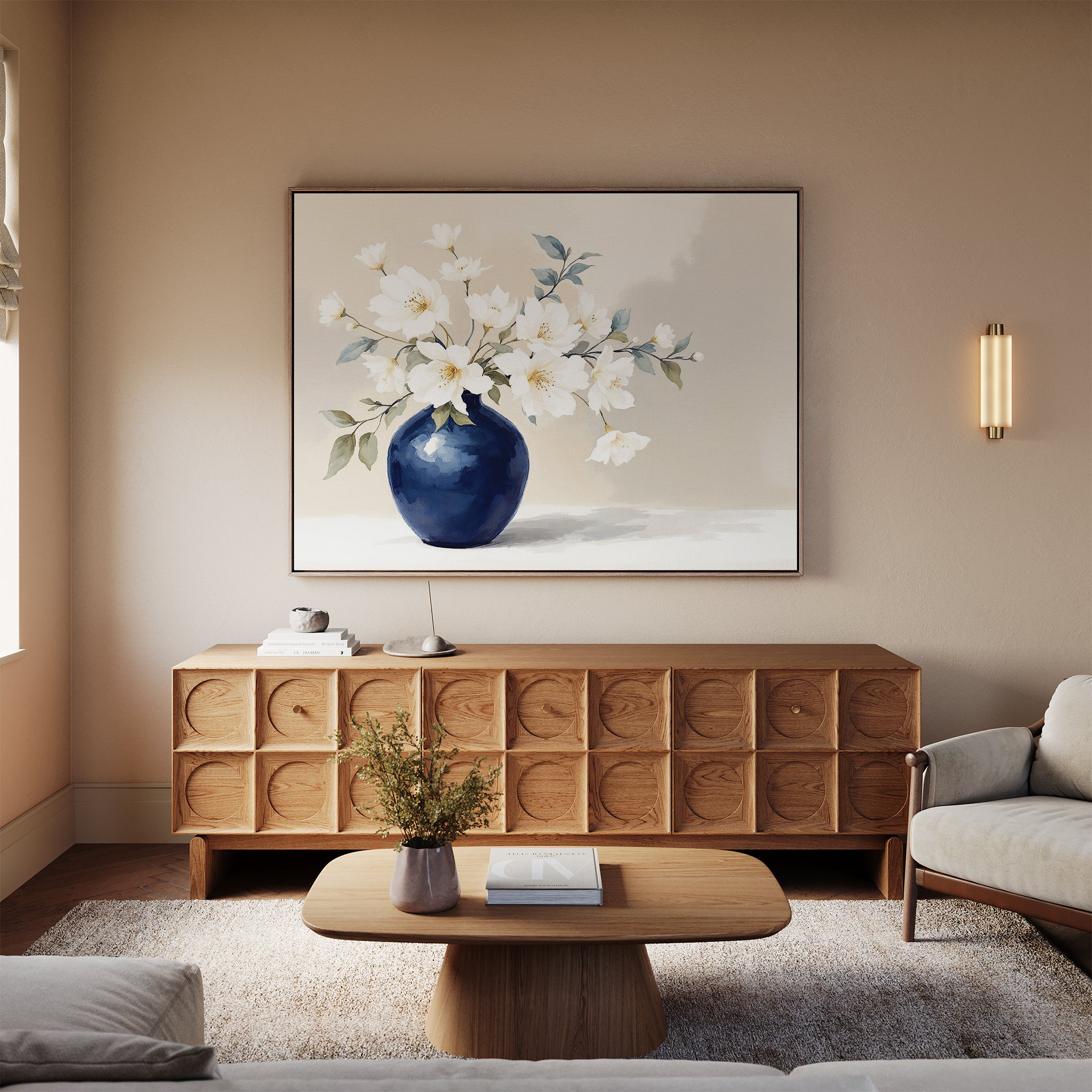 A modern living room featuring the Porcelain Dreams Canvas Art - Horizontal depicting white flowers in a blue vase, a wooden sideboard, light wood coffee table with flowers, sofa, neutral walls, and a wall sconce.