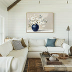 A cozy living room with a white sectional, blue accent pillows, and a wooden coffee table. The "Porcelain Dreams Canvas Art - Horizontal" adds floral artistry to the white shiplap wall with its depiction of white flowers in a blue vase.
