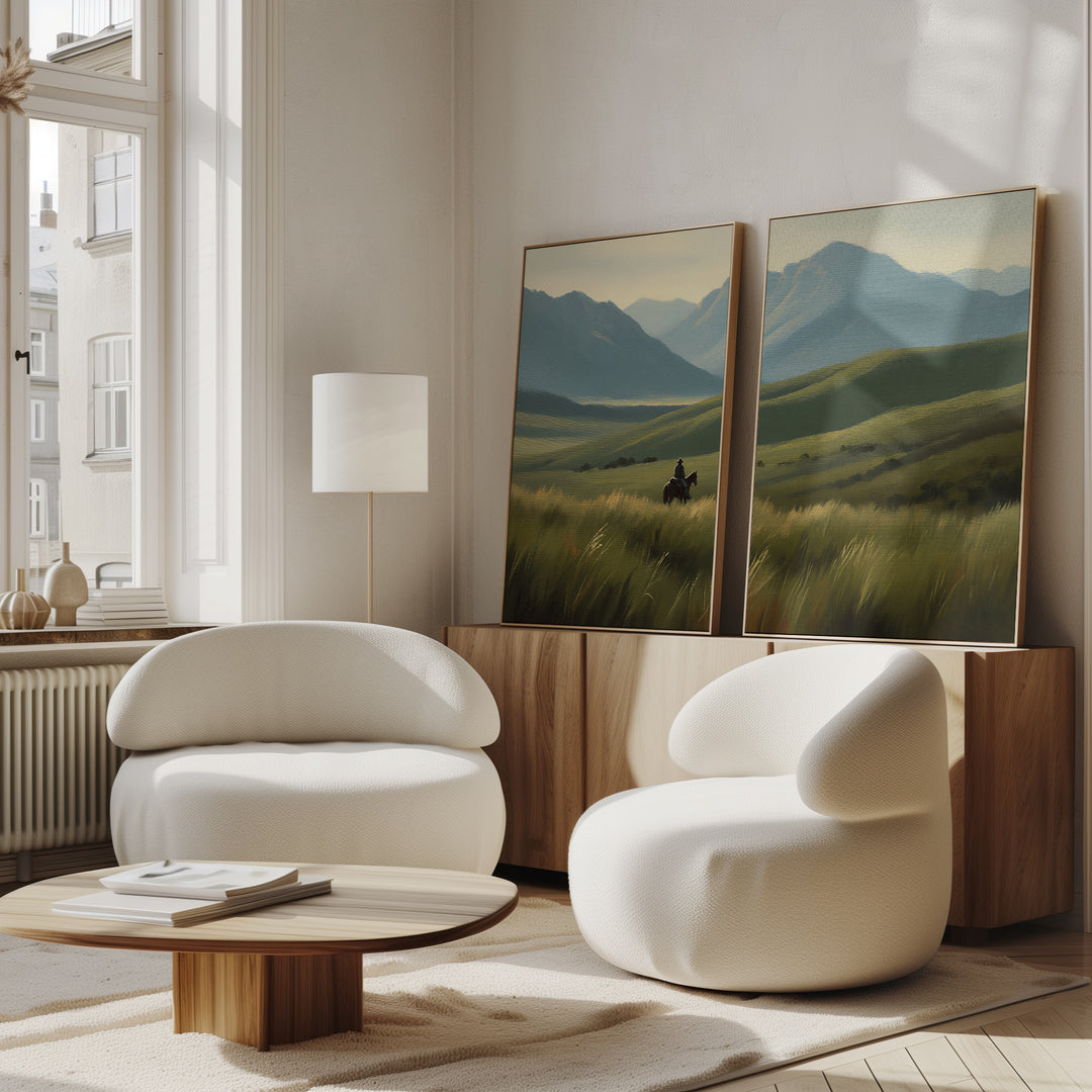 A modern living room with two white, rounded armchairs, a low wooden table, and western wall art—Prairie Wanderer - Set of 2 canvas prints of green hills and mountains on a wooden sideboard beneath large windows.