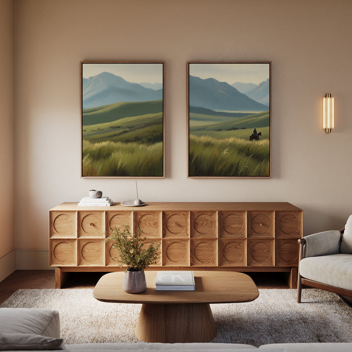 A cozy living room with a modern wooden sideboard, coffee table, light sofas, a small plant, and the Prairie Wanderer - Set of 2 canvas prints of green hills and mountains on the wall above the sideboard.