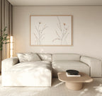 A minimalist living room features a light beige sectional sofa, a low wooden coffee table with a black bowl, neutral walls, and the Prairie Whispers Canvas Art - Horizontal as botanical artwork, bathed in soft natural light for tranquil ambiance.