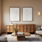 A cozy living room features a wooden coffee table, modern sideboard, flower vase, beige armchair, and two botanical wall art prints—Prairie Whispers - Set of 2—all styled in warm neutral tones.