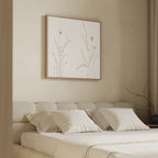 A minimalistic beige bedroom features a low bed with cream bedding and the Prairie Whispers Canvas Art - Square, showcasing delicate botanical flowers, hanging above the headboard.