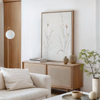 A minimal, modern living room with a white sofa, wooden sideboard topped with beige vases and books, a potted plant, and the Prairie Whispers Canvas Art - Vertical. Neutral tones and soft lighting create a tranquil, natural atmosphere.