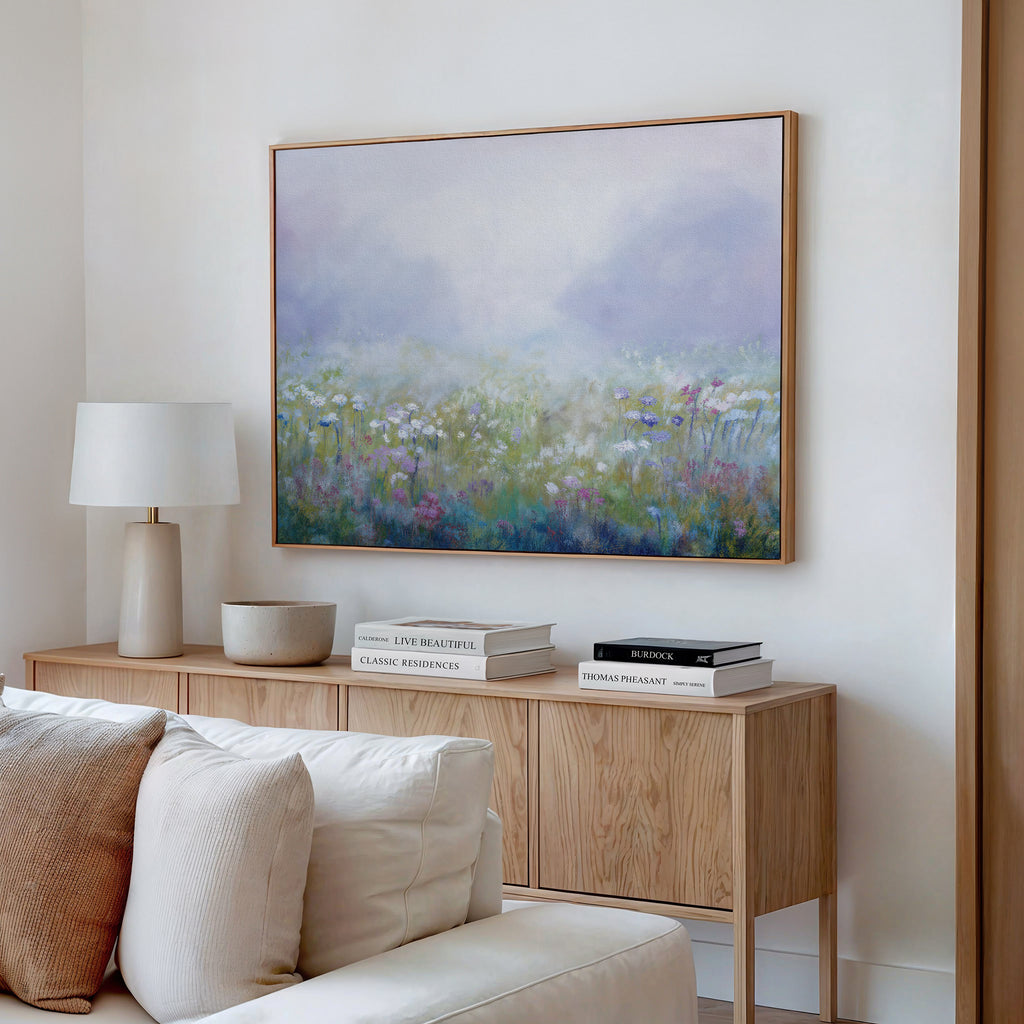 A cozy living room with a light wood console table, stacked books, a white lamp, and the Purple Haze Canvas Art - Horizontal above—perfect inspiration for stylish decor.