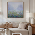 A cozy living room featuring a beige sofa with cushions, a lamp on a wooden side table, dried flowers in a vase, and the Purple Haze Canvas Art - Square—an ideal piece to add charm to your decor.