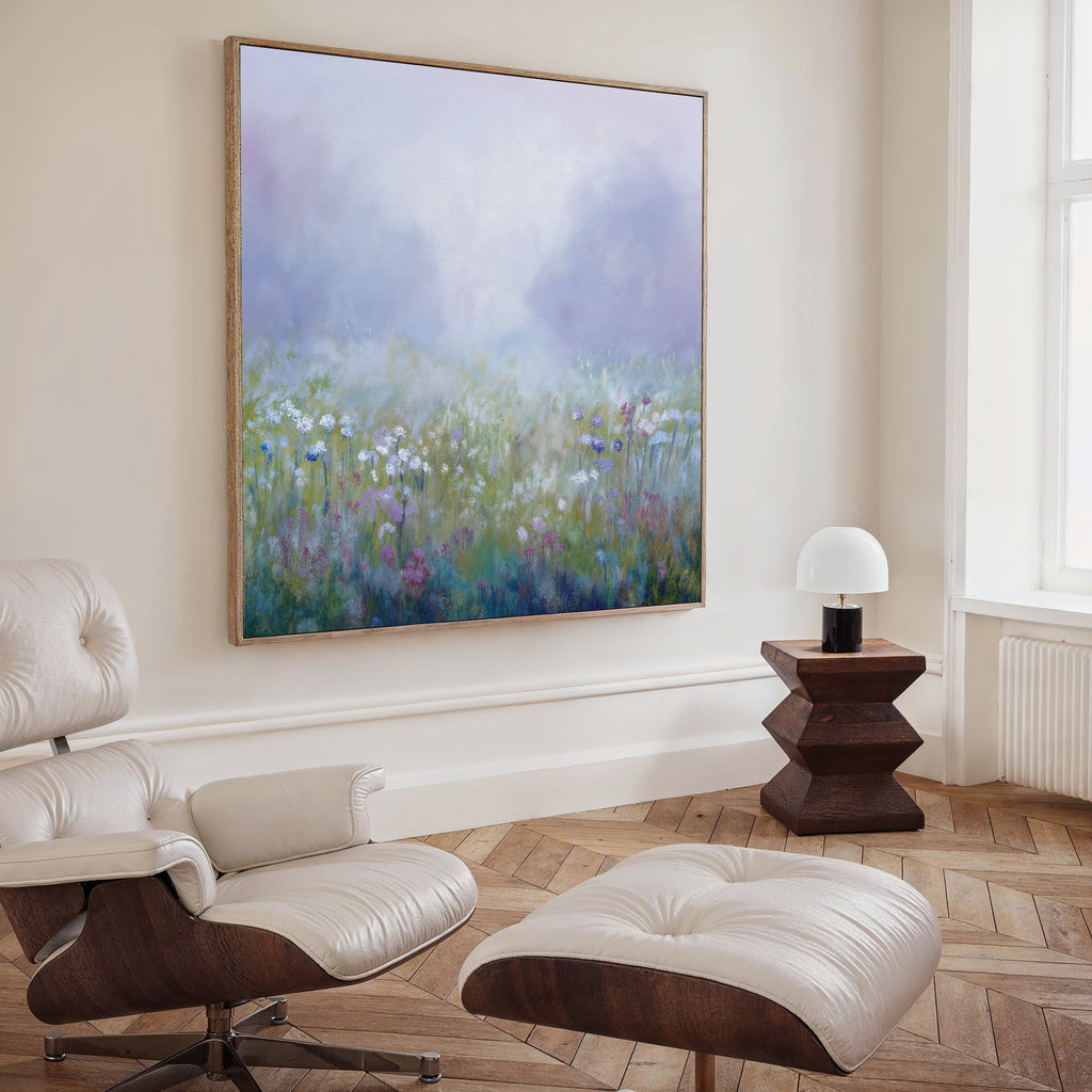 A modern living room features a white leather lounge chair and ottoman, an angular dark wood side table with a white lamp, and the Purple Haze Canvas Art - Square on a beige wall—perfect for stylish living room decor.