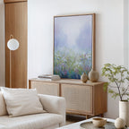 A modern living room featuring the Purple Haze Canvas Art - Vertical, a light wood sideboard, neutral ceramics, stacked books, a white sofa with cream pillow, globe pendant light, and a small potted green plant.