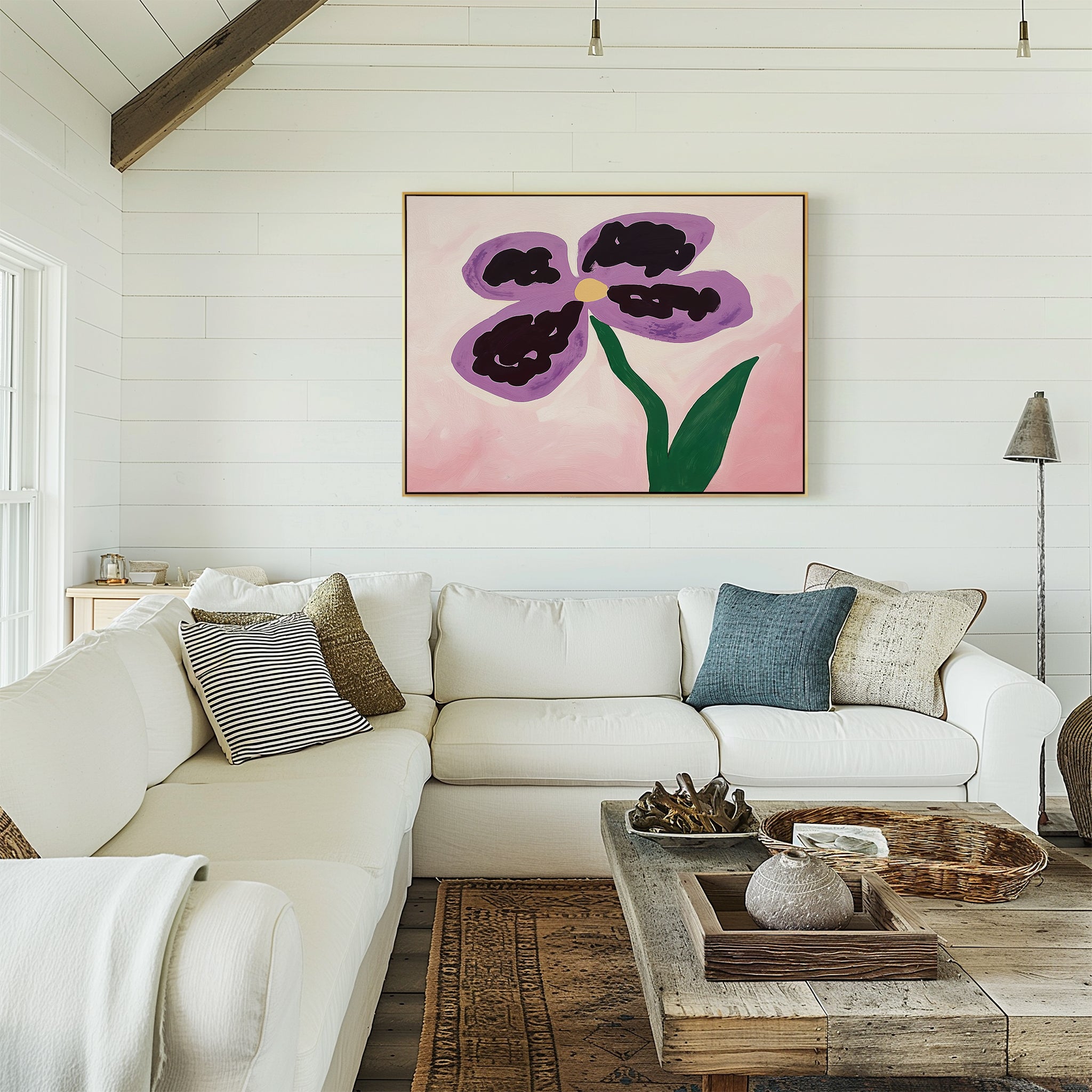 A cozy living room with white shiplap walls, a white sectional sofa, assorted pillows, a rustic wooden coffee table, and the Purple Pansy Canvas Art - Horizontal featuring a large purple and yellow flower.