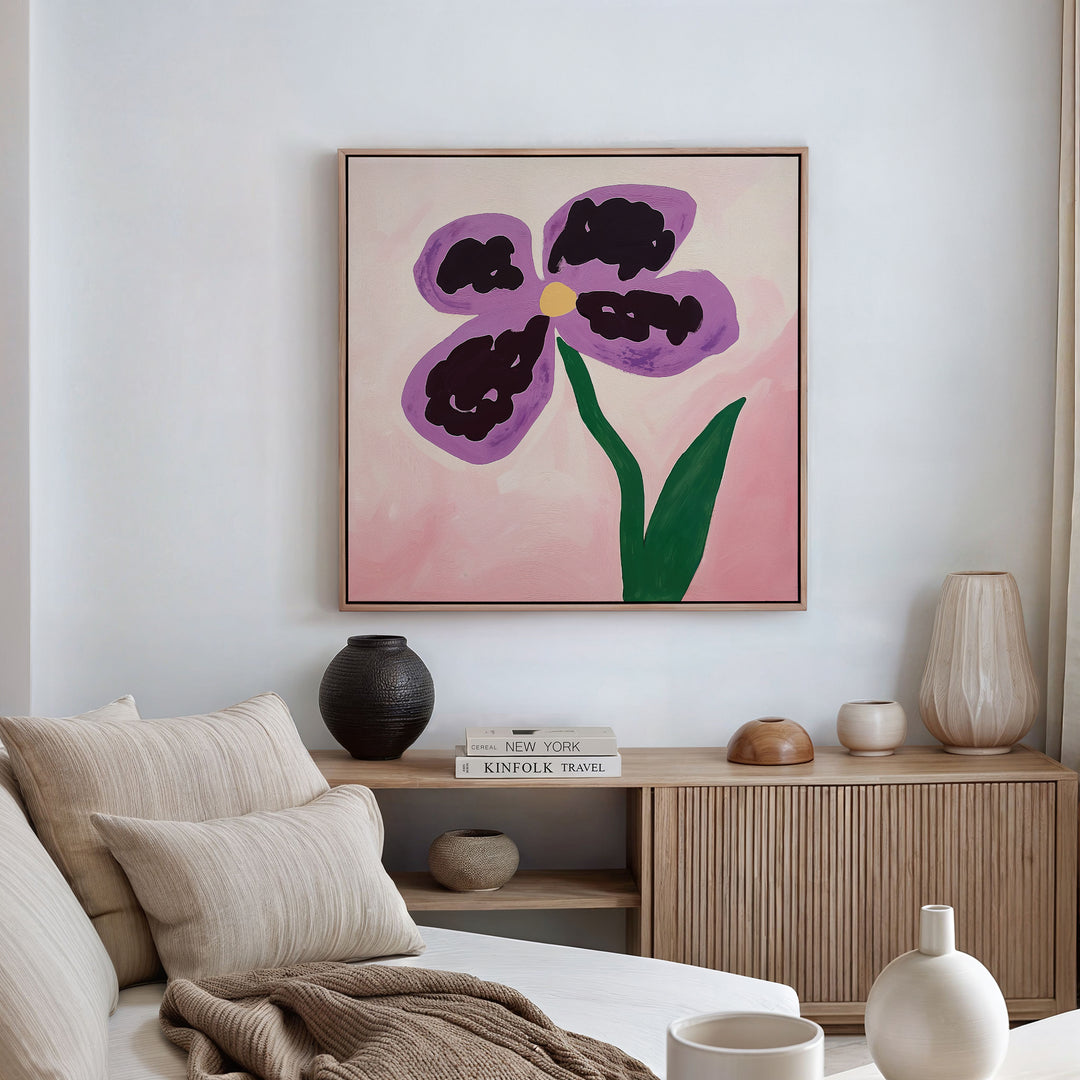 A minimalist living room with a beige sofa, neutral cushions, and a wooden console. The Purple Pansy Canvas Art - Square hangs above, adding Nordic Park-inspired charm. Decorative vases and books line the console table.