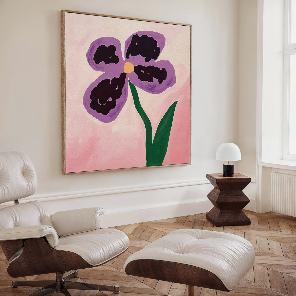 A modern living room with a white leather lounge chair and ottoman, dark wood side table with a white lamp, and the Purple Pansy Canvas Art - Square featuring a large botanical print on a pink background.